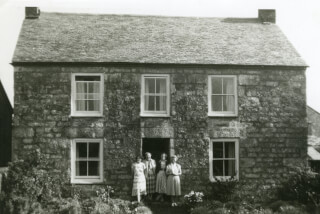 grayscale-photo-of-four-women-standing-in-front-of-house