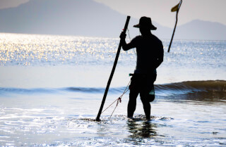man-fishing-on-shallow-waters-of-the-beach-against-the-light
