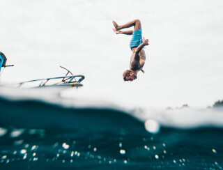 man-wearing-blue-shorts-about-to-dive-on-body-of-water