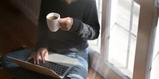 woman-using-laptop-while-holding-a-cup-of-coffee